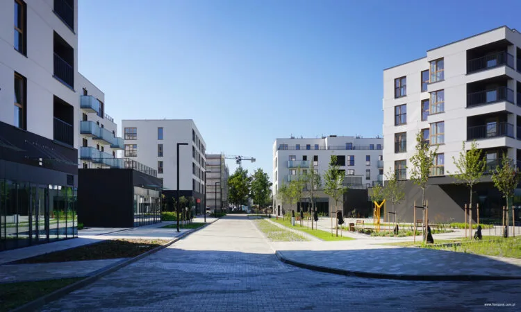Osiedle ATAL Nowe Miasto Polesie etap 3 - elewacja budynku z balkonami oraz lokalami usługowymi w parterze, widok od ulicy, strefa piesza z zielenią, ławkami oraz latarniami.
